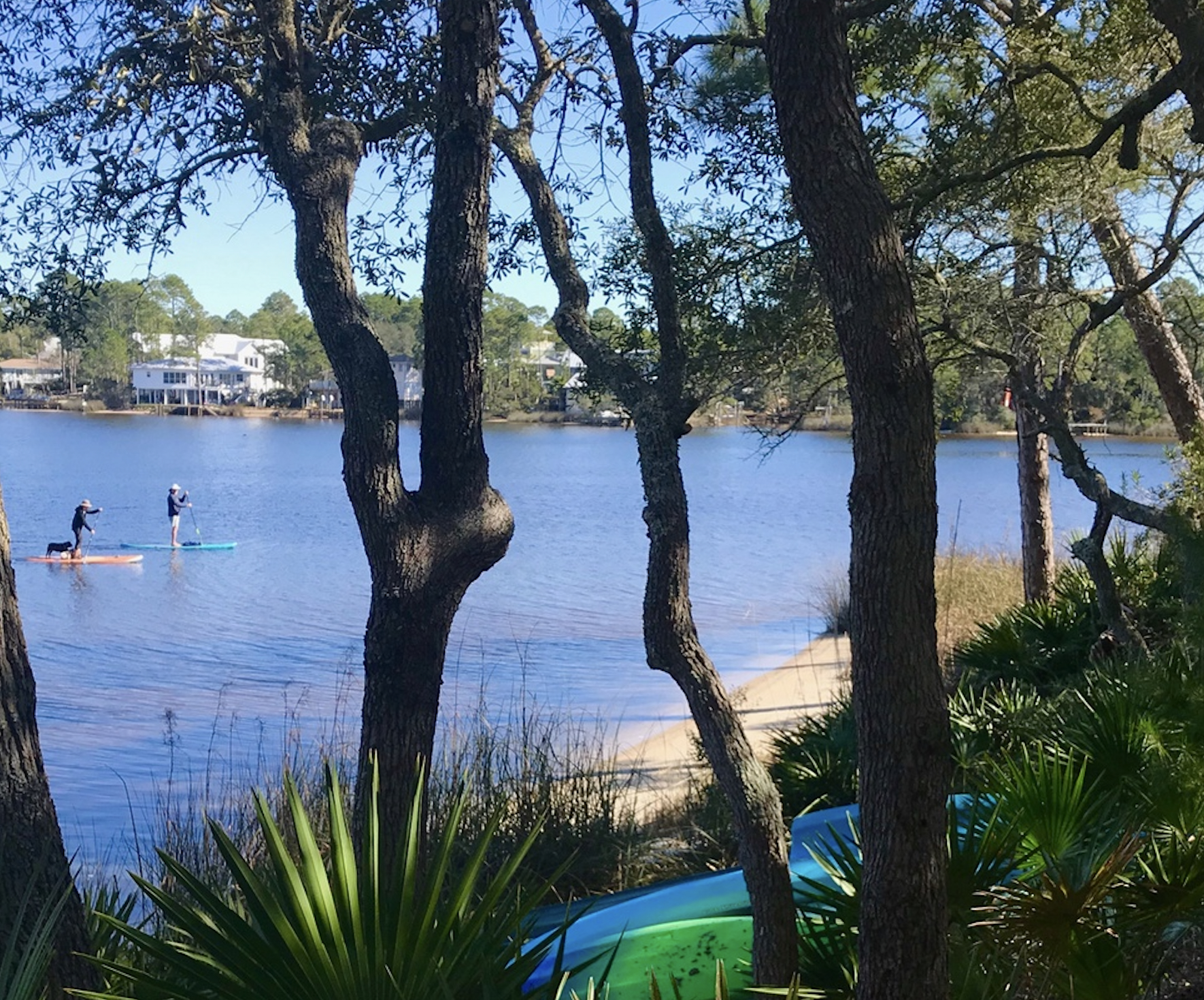 On 30A's Eatern Lake, a couple paddleboard in front of SeaGroovin', an Oversee Vacation Home.